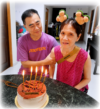 A man and woman are sitting at a table with a cake with lit candles. Description generated by AI