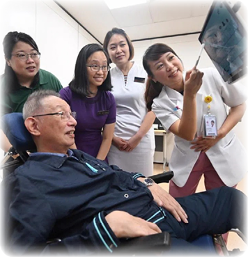A man in a wheelchair is being shown something on a tablet by a group of women. Description generated by AI