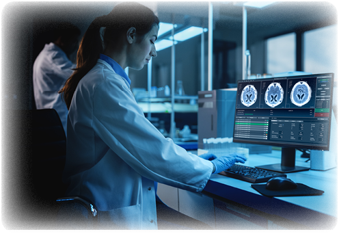A person wearing a lab coat and gloves is seated at a desk in a laboratory, analyzing brain scan images displayed on a computer monitor. Description generated by AI